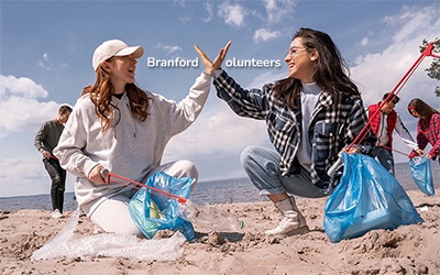 Volunteers high-five while picking up trash from a beach
